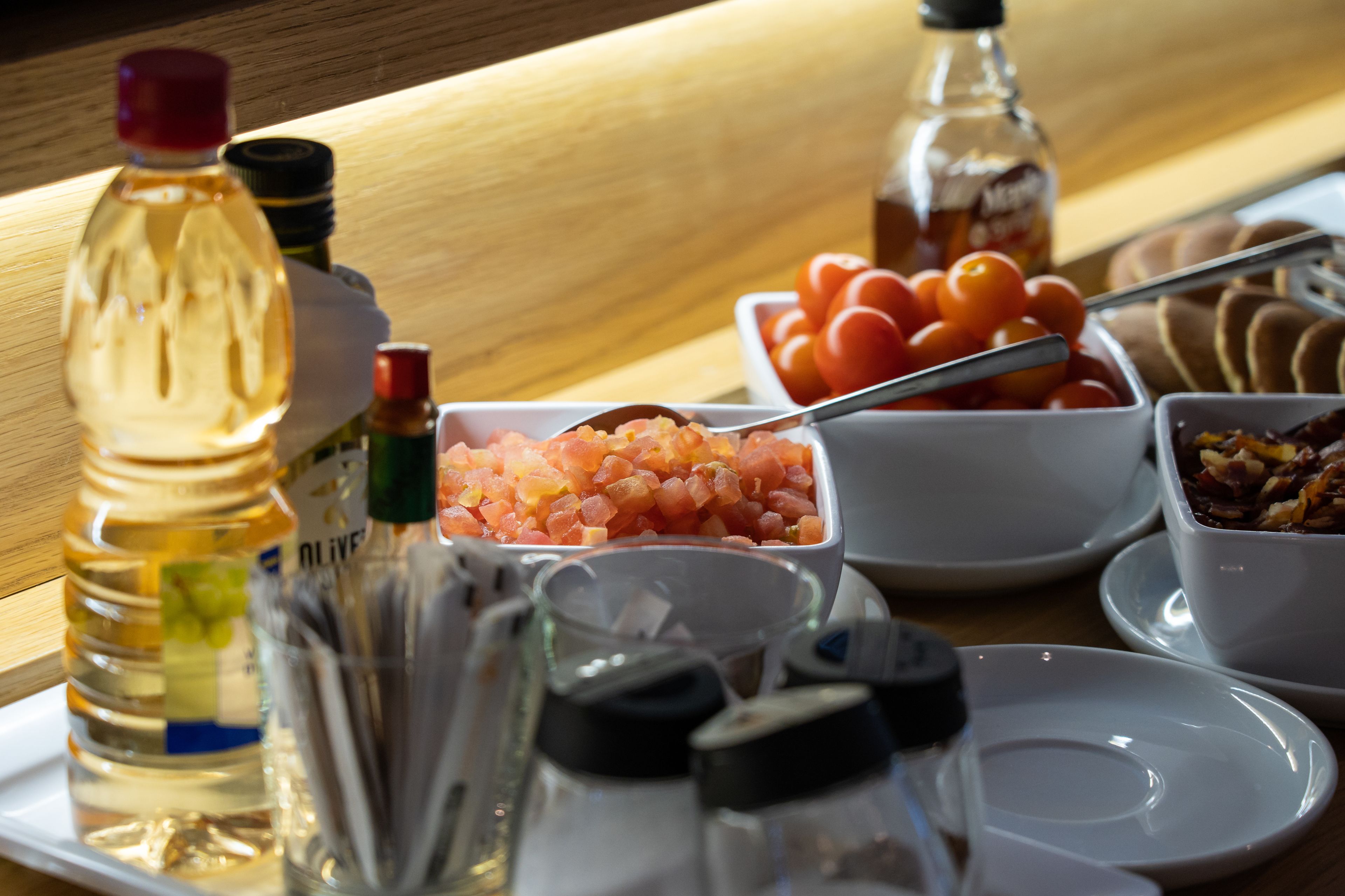 A table with various condiments and snacks, including olives, tomatoes, and pickles.