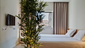 A hotel room with a bed, a TV mounted on the wall, and a large potted plant. - Hotel Spot Family Suites (Porto)