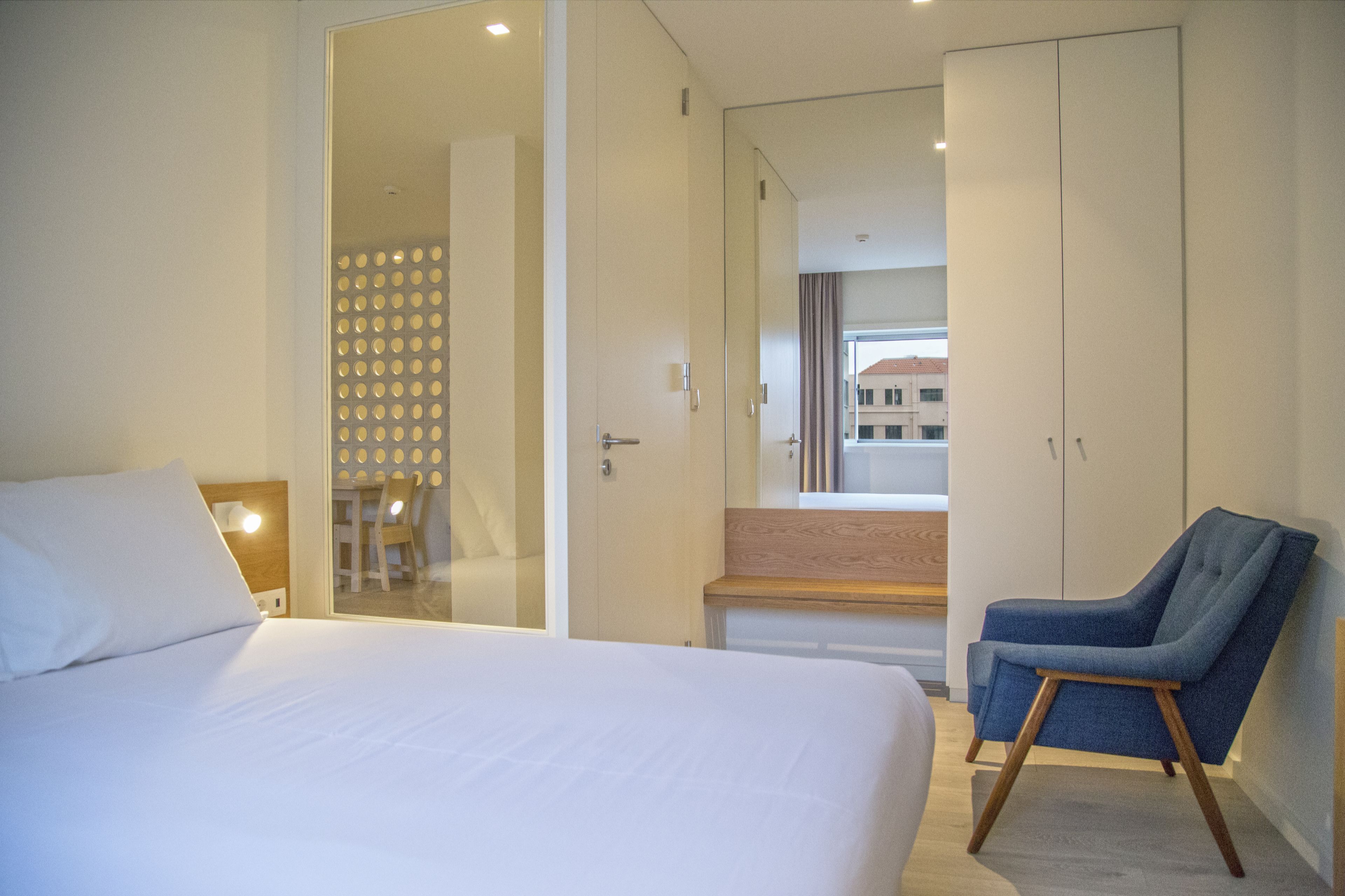 Quarto de hotel moderno com uma cama grande, um espaço de estar com uma poltrona e vista para o exterior.