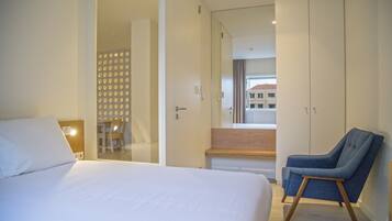 Quarto de hotel moderno com uma cama grande, um espaço de estar com uma poltrona e vista para o exterior.