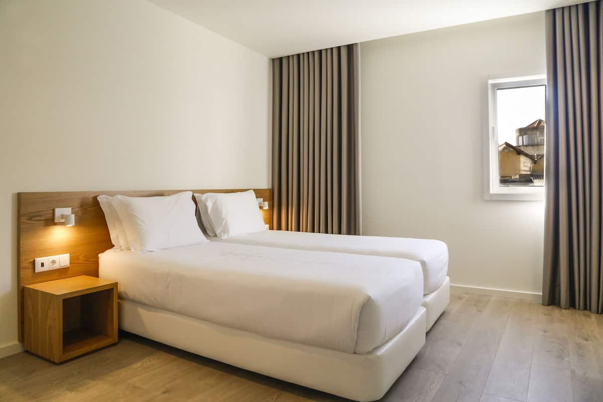 A modern hotel room with a large bed, a wooden nightstand, a window with curtains, and a vertical striped wall.