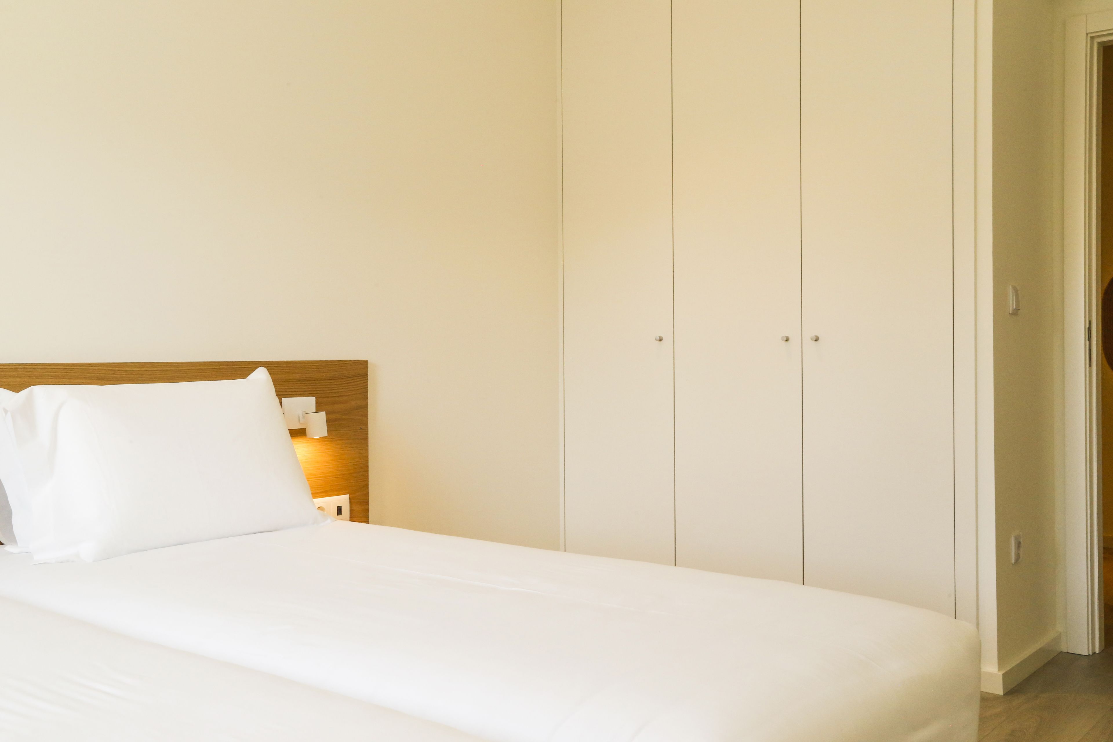 A bedroom with a bed, a nightstand, a wardrobe, and a door leading to another room.