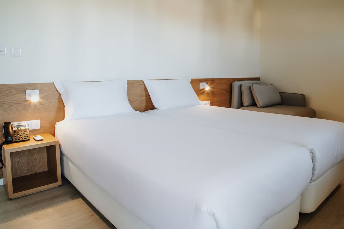 A hotel room with a large bed, two bedside tables, a bedside phone, and a nightstand.