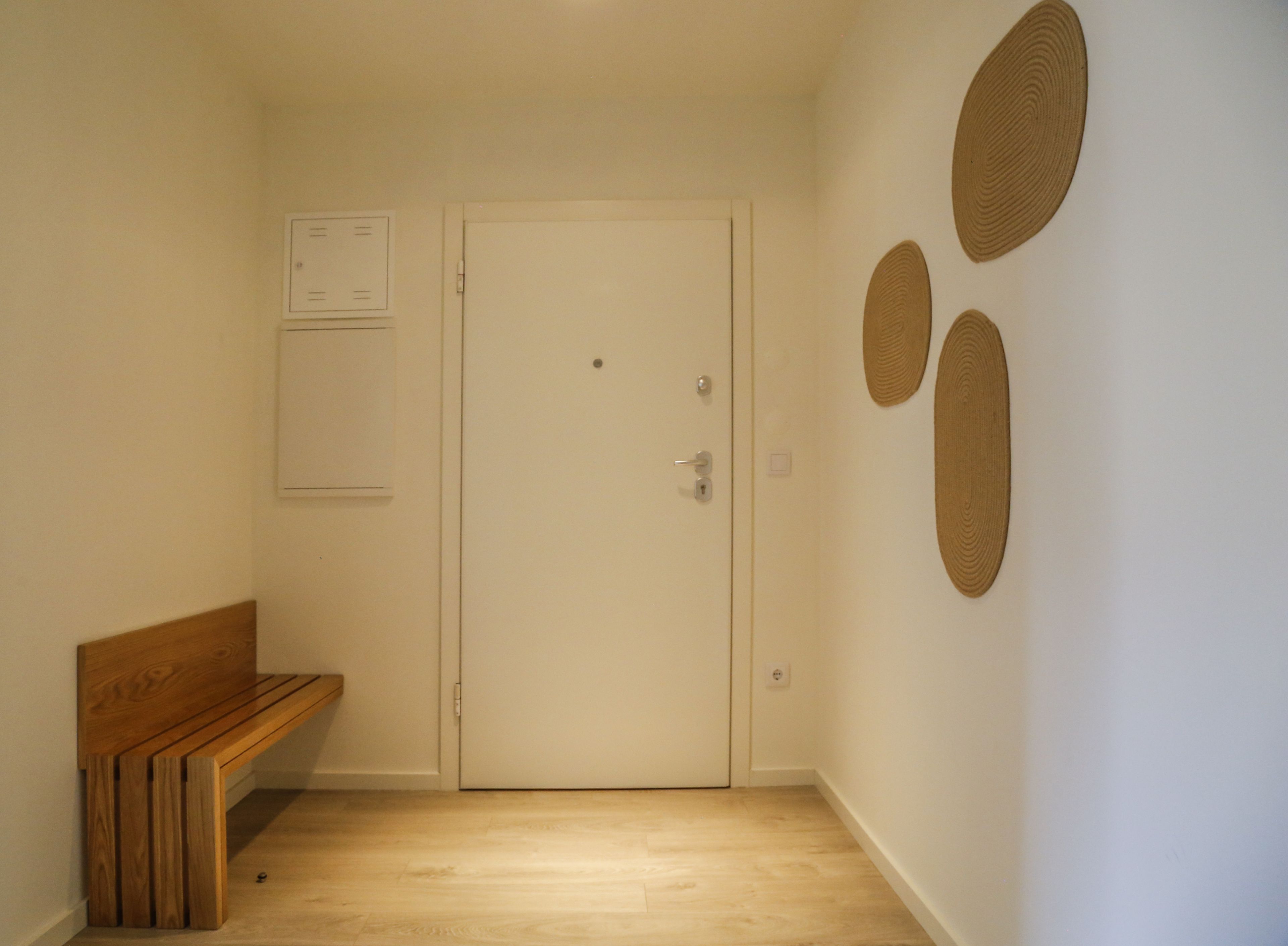 Un couloir avec un banc en bois, une porte blanche et des décorations circulaires fixées au mur.