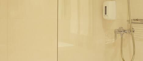 A shower area with a glass partition, a handheld showerhead, and a wall-mounted control panel.