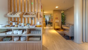 A modern hotel lobby with wooden paneling, a seating area with sofas, and a buffet with various food items and glassware. - Hotel Spot Family Suites (Porto)