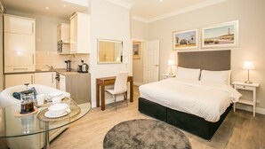 Une chambre d’hôtel moderne équipée d’un lit, de tables de chevet, d’un bureau et d’une table en verre avec une cafetière.