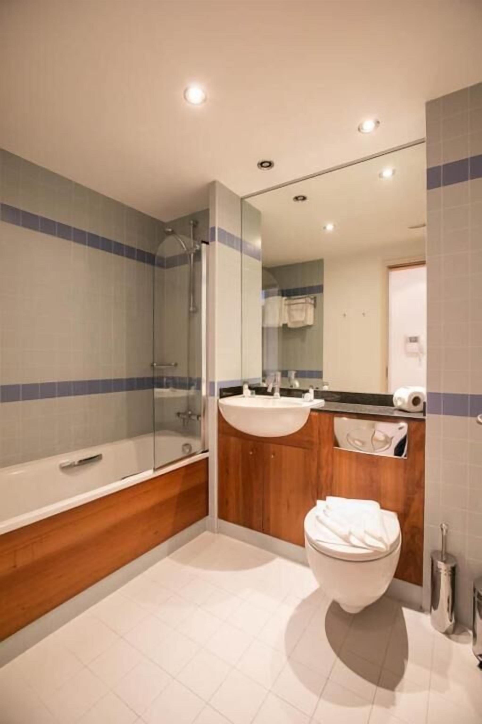 Un baño moderno con ducha envuelta en vidrio, tocador de madera y un inodoro blanco.