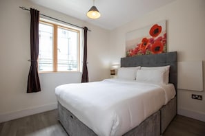 A bedroom with a large bed, a window with curtains, a painting on the wall, and a lamp. - Grand Canal District Apartments (Dublin)