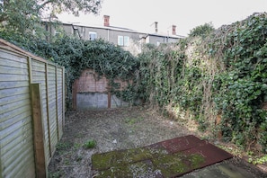 A backyard with a wooden fence, a brick wall, and dense ivy growth. - Grand Canal District Apartments (Dublin)