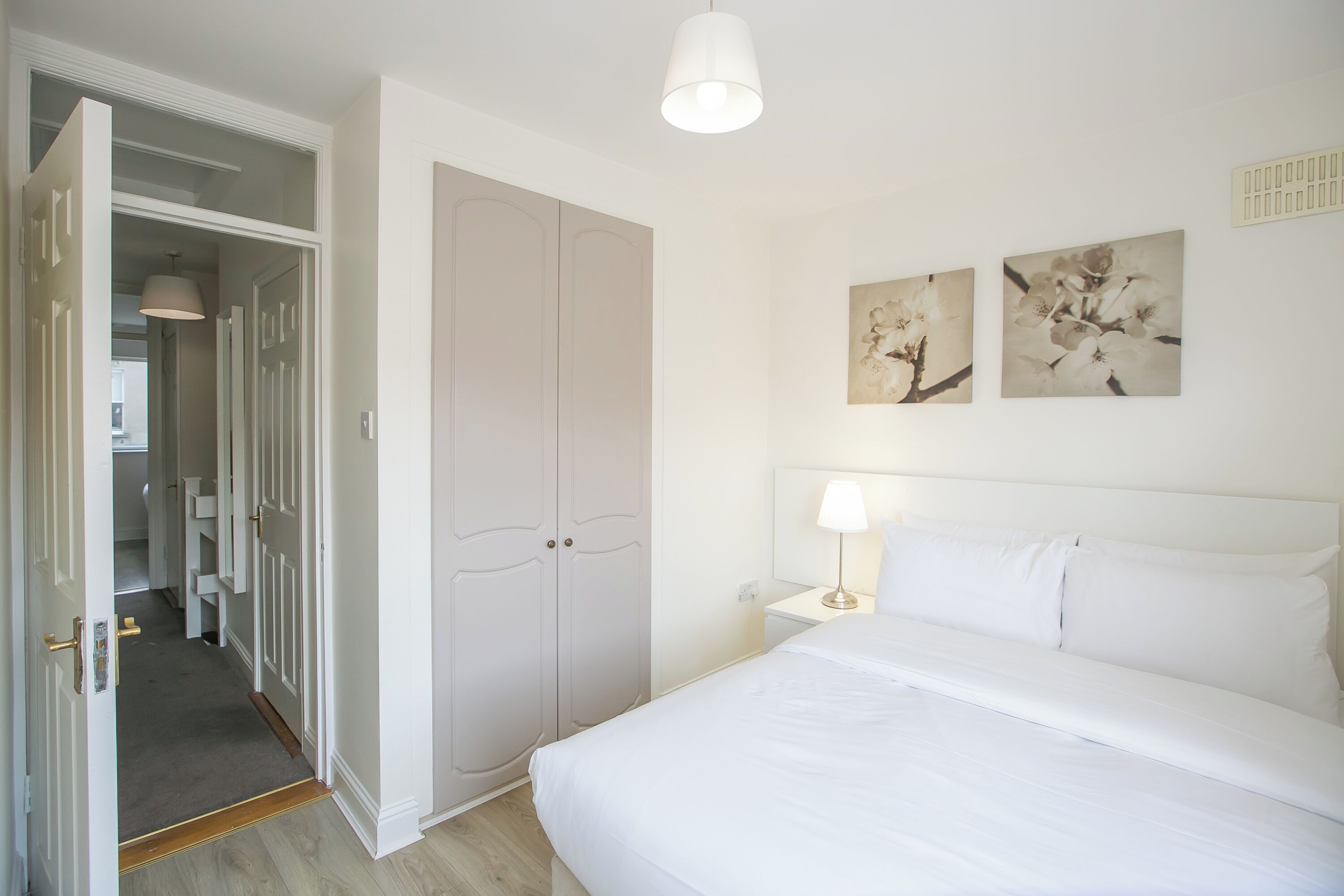 A bedroom with a bed, a nightstand, a lamp, and two wall-mounted paintings.