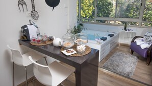 Eine moderne Küche mit dunkler Arbeitsplatte, weißen Stühlen und Blick auf Bäume durch große Fenster.