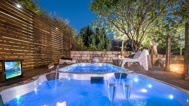 Ein Whirlpool mit zwei Sektgläsern, Kerzen und einem Fernseher in einem Garten.