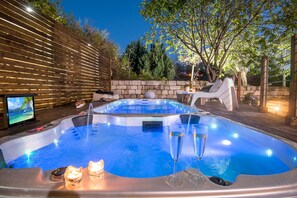 A hot tub with two glasses of champagne, candles, and a television in a backyard setting. - Osnata Boutique Suites (Kfar Vradim)