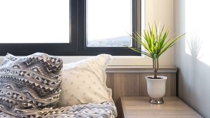 A bed with patterned bedding, a bedside plant, and a window with a view. - Oslo Hostel Rønningen (Oslo)