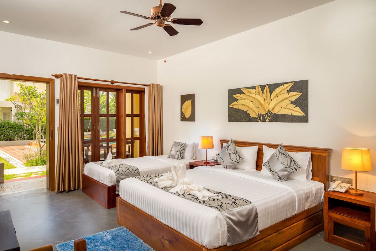 A hotel room with two beds, a ceiling fan, and a view of the outdoors.