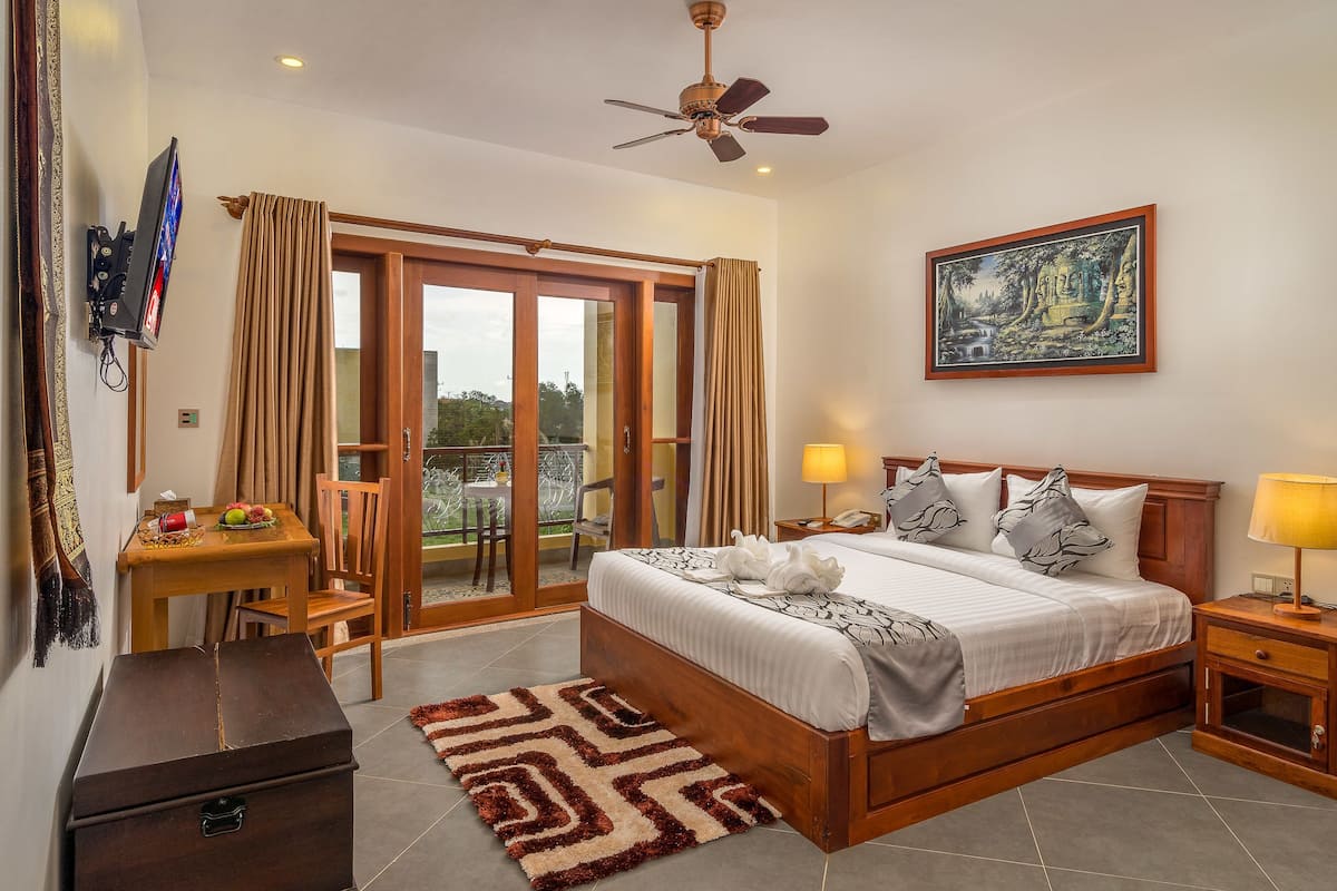 A bedroom with a bed, bedside tables, a desk with a chair, a television, and a balcony door.