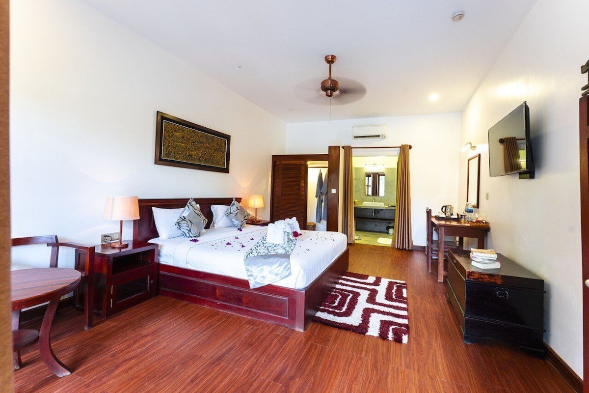 A hotel room with a bed, bedside table, lamp, and a small desk with a chair.