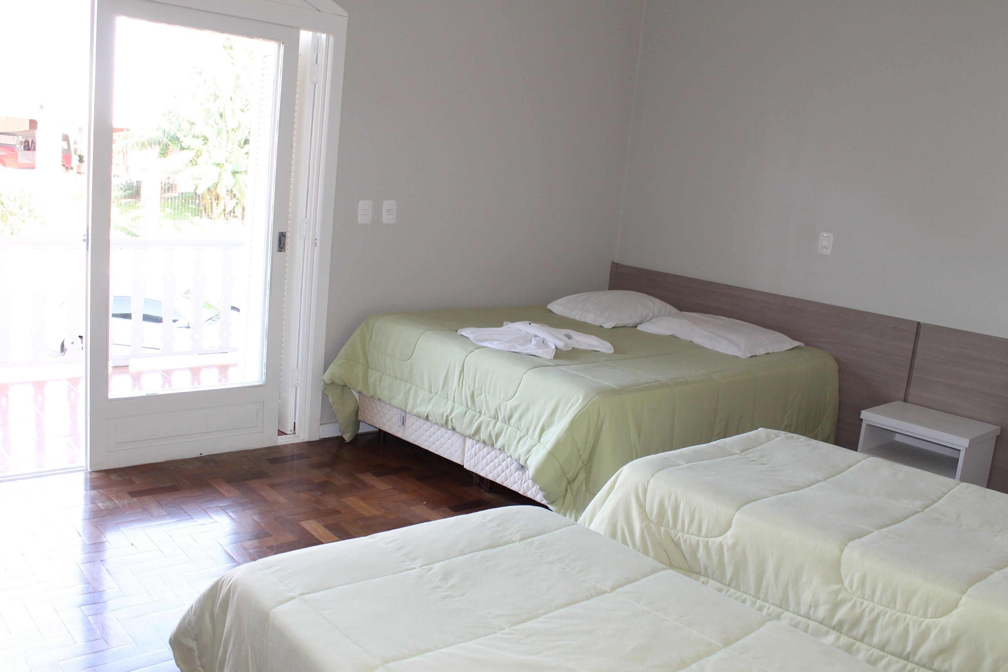 A hotel room with two beds, a wooden floor, a sliding glass door, and a small bedside table.