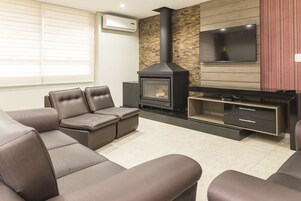 Uma sala de estar moderna com lareira, sofás de couro, televisão de tela plana e uma parede de destaque em madeira.