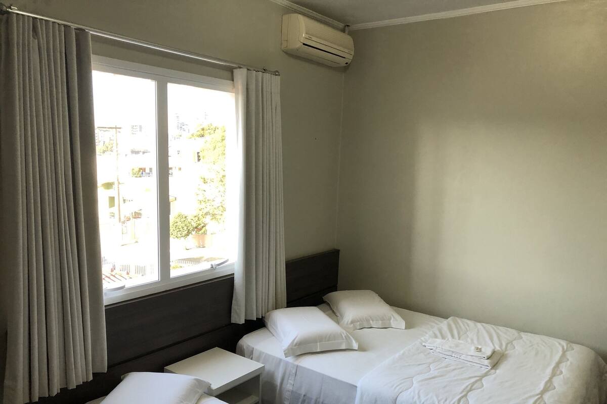 A hotel room with two single beds, a small table, and a window with curtains.