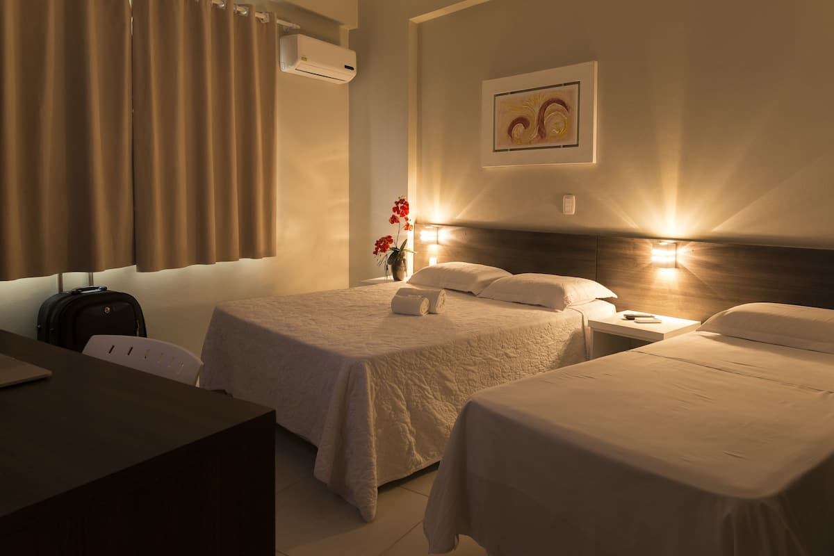 A hotel room with two beds, a desk, a chair, and a wall-mounted air conditioner.