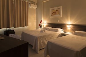 Quarto de hotel com duas camas, uma mesa, uma cadeira e ar condicionado fixado na parede.