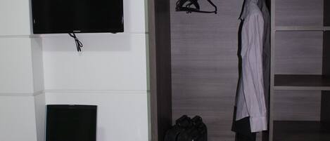 A hotel room with a desk, a laptop, a television, a mini-fridge, a wardrobe, and an air conditioning unit.