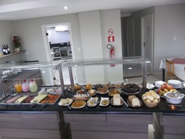 Buffet com diversos tipos de comida e área de cozinha ao fundo.