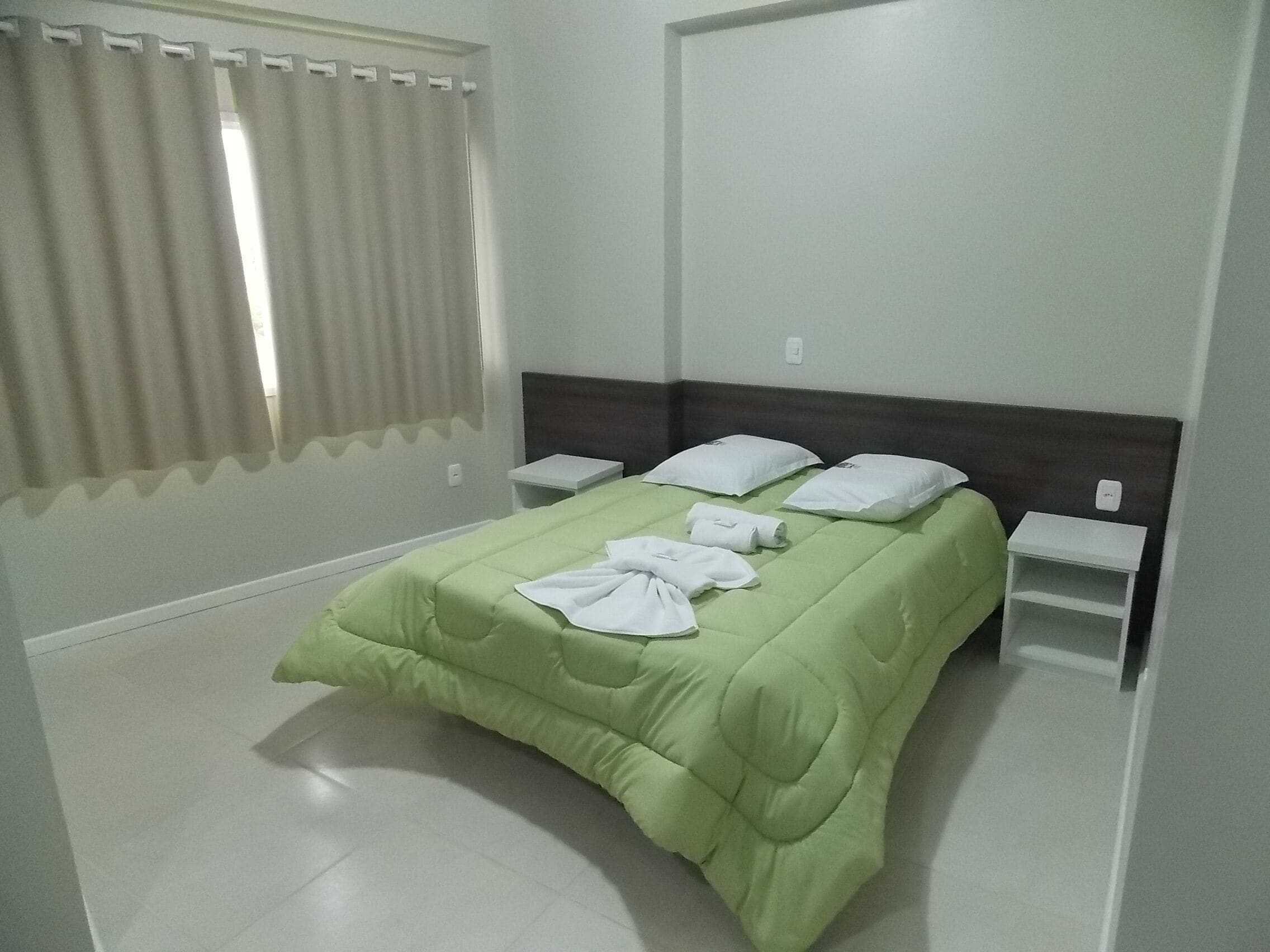 A hotel room with a green bedspread, white pillows, and a neatly made bed.