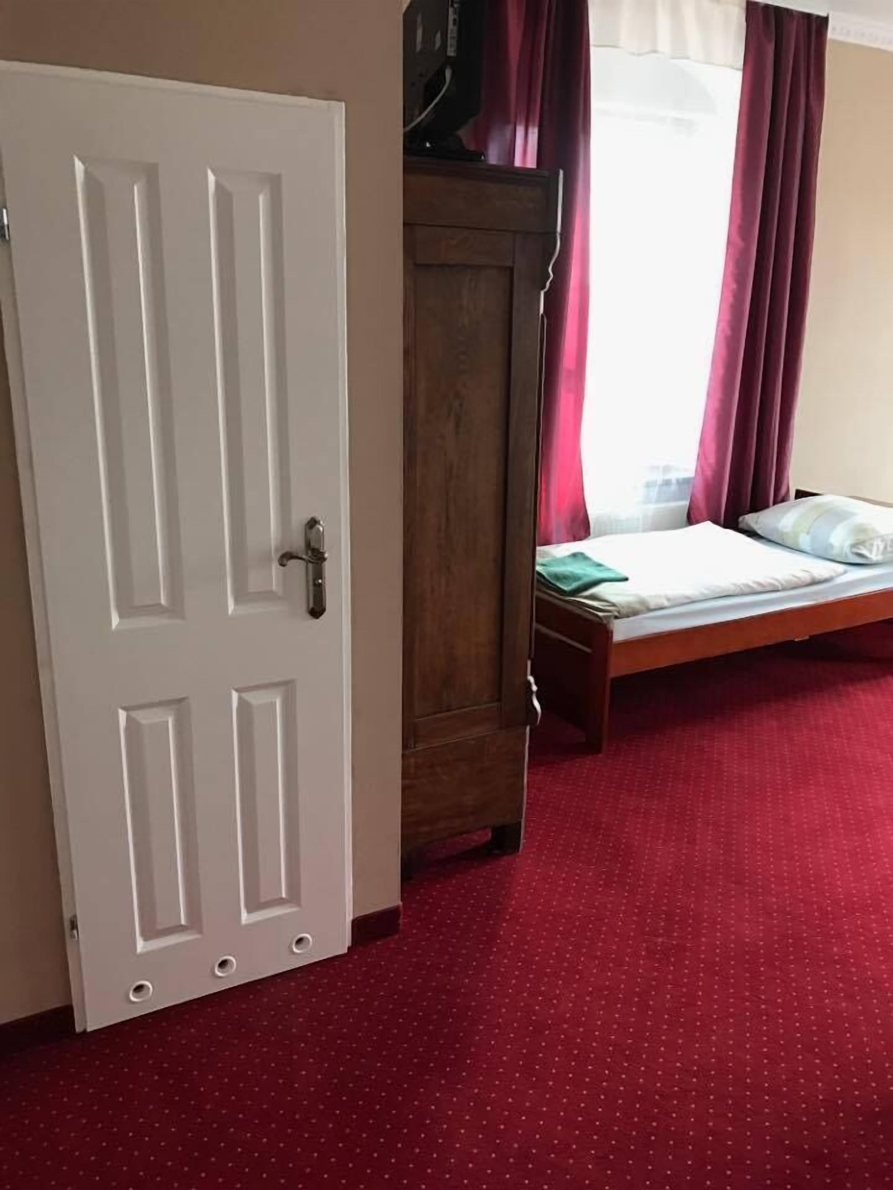 A room with a wooden wardrobe, a bed with a green blanket, and a red carpet.
