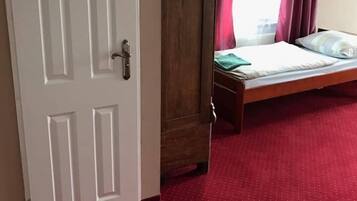 A room with a wooden wardrobe, a bed with a green blanket, and a red carpet.