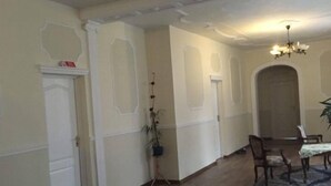 A spacious room with a wooden floor, white walls, and a chandelier. There is a dining table with chairs and a potted plant. - Palac Lasow (Piensk)