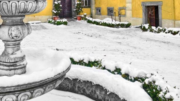 A courtyard with a fountain, a yellow building with a purple door, and snow on the ground. - Palac Lasow (Piensk)