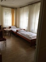 Una habitación con dos camas individuales, una mesita pequeña y una silla.