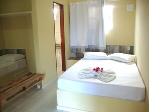 A single-bed room with a wooden bench, a bathroom visible through a door, and a window with a curtain. - Pousada O Tabuleiro (Conde)