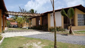 Um edifício residencial com um pátio ladrilhado, uma pérgula e um jardim com palmeiras e flores.