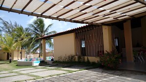 Uma área de varanda coberta com piscina, palmeiras e um jardim com flores cor-de-rosa.