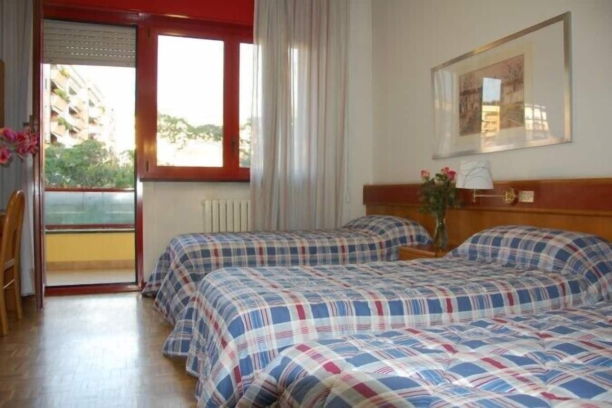 A hotel room with two beds, a window with curtains, a radiator, a wooden headboard, and a framed picture on the wall.