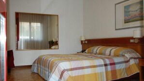 Een slaapkamer met een bed, een groot raam met gordijnen, een nachtkastje met een lamp en een lijst met een afbeelding aan de muur.