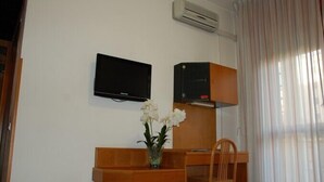 Hotelkamer met een bed, een houten bureau, een aan de muur bevestigde televisie, een airconditioning en een raam met gordijnen.