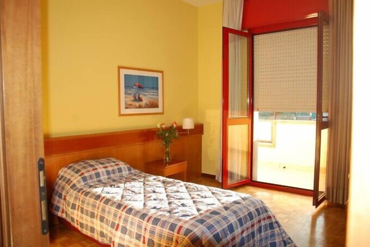 A bedroom with a bed, a nightstand, a framed picture, and a sliding glass door to a balcony.