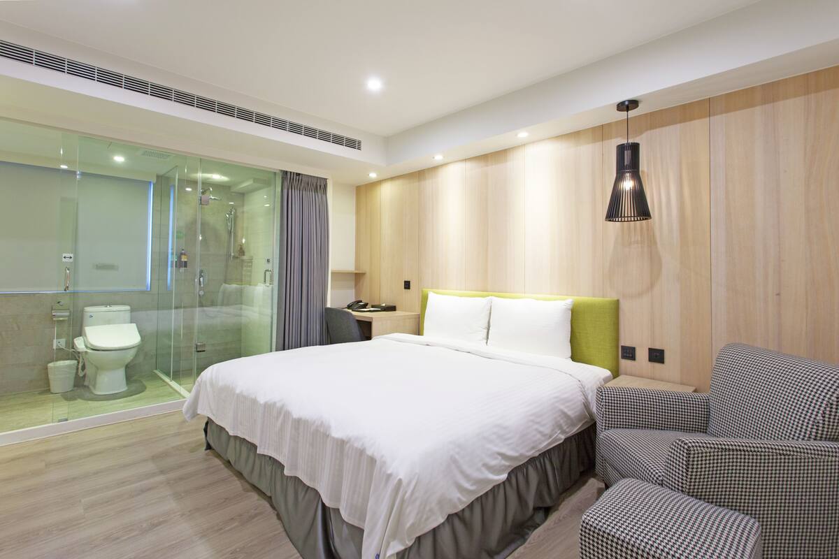 Une chambre d’hôtel moderne dotée d’un grand lit, d’une douche en verre et d’un coin salon avec un canapé à motifs à carreaux.
