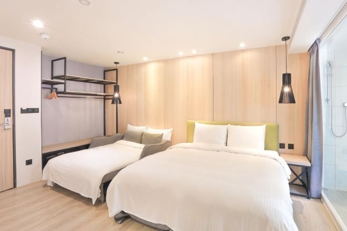 Una habitación de hotel moderna con dos camas, un panel de pared de madera, un banco empotrado y zona de ducha.