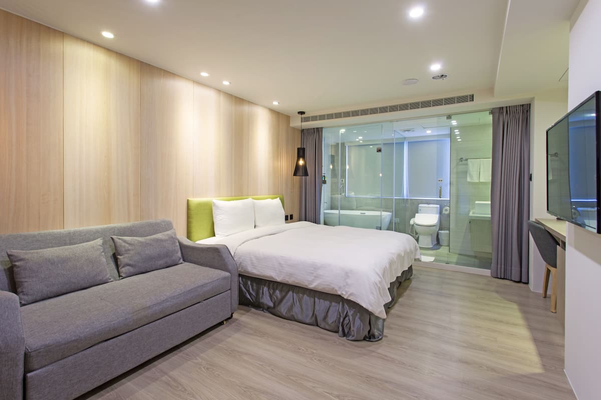 Une chambre d’hôtel moderne équipée d’un lit, d’un canapé, d’une télévision et d’une douche en verre.