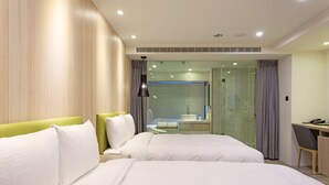 A hotel room with two beds, a desk, and a bathroom visible through a glass partition.