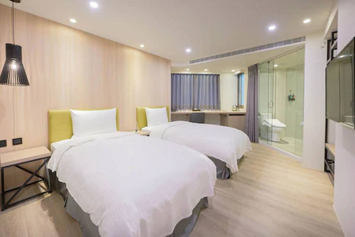 Une chambre d’hôtel avec deux lits, un bureau, un espace douche et un grand miroir.