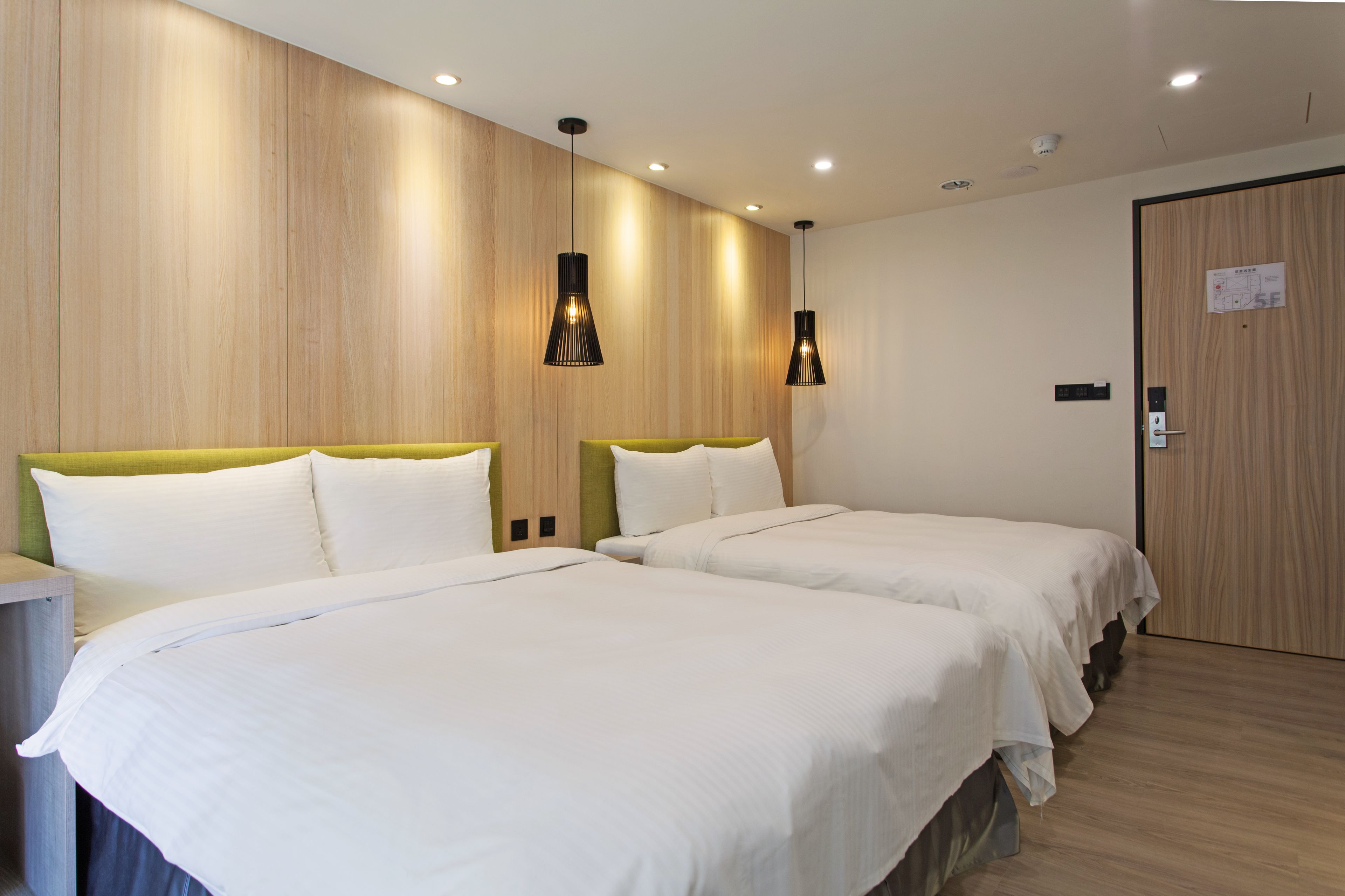 A hotel room with two beds, wooden panel walls, and pendant lighting.