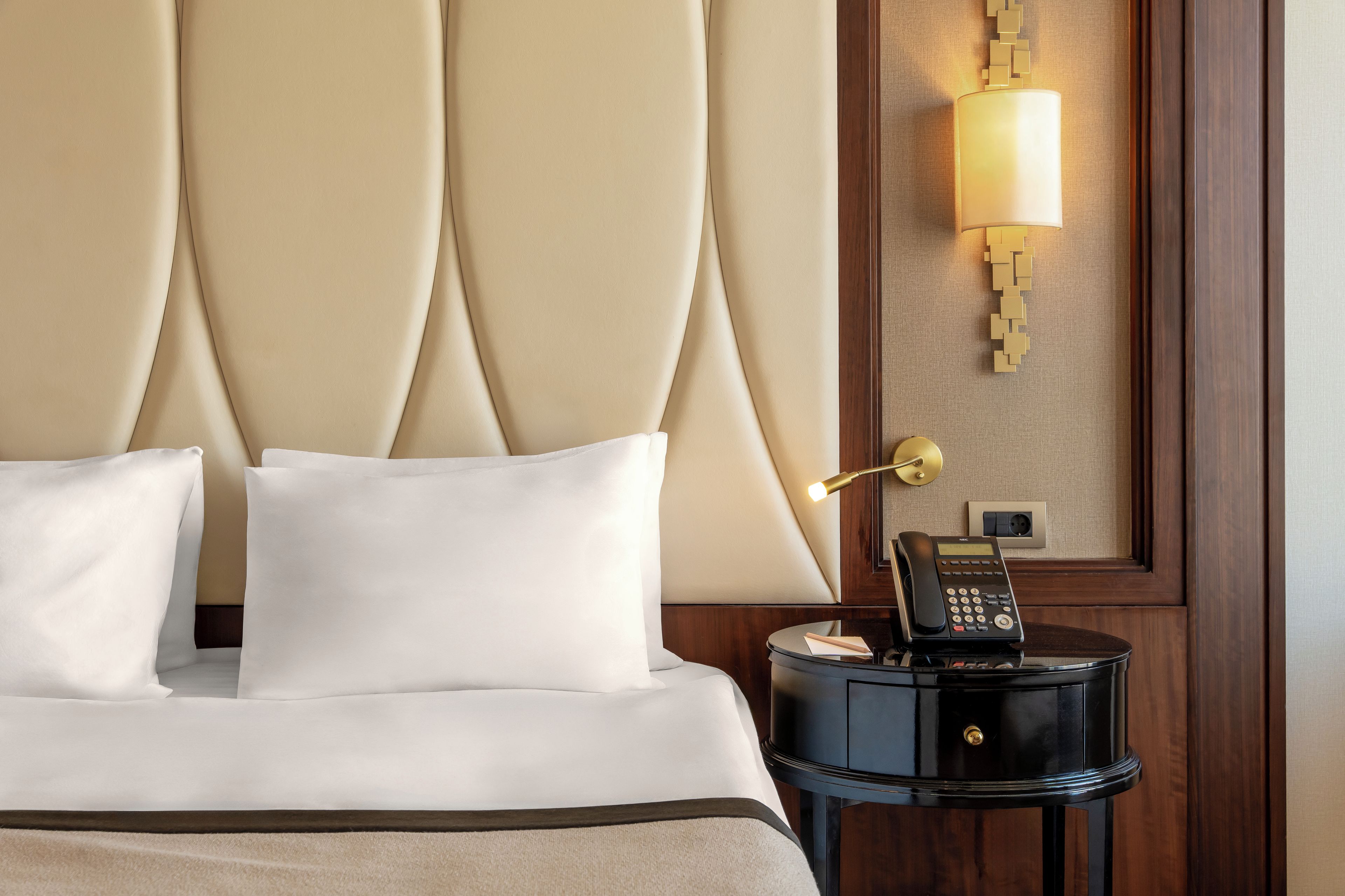 Een hotelkamer met een bed, kussens, een nachtkastje met een lamp en een telefoon.