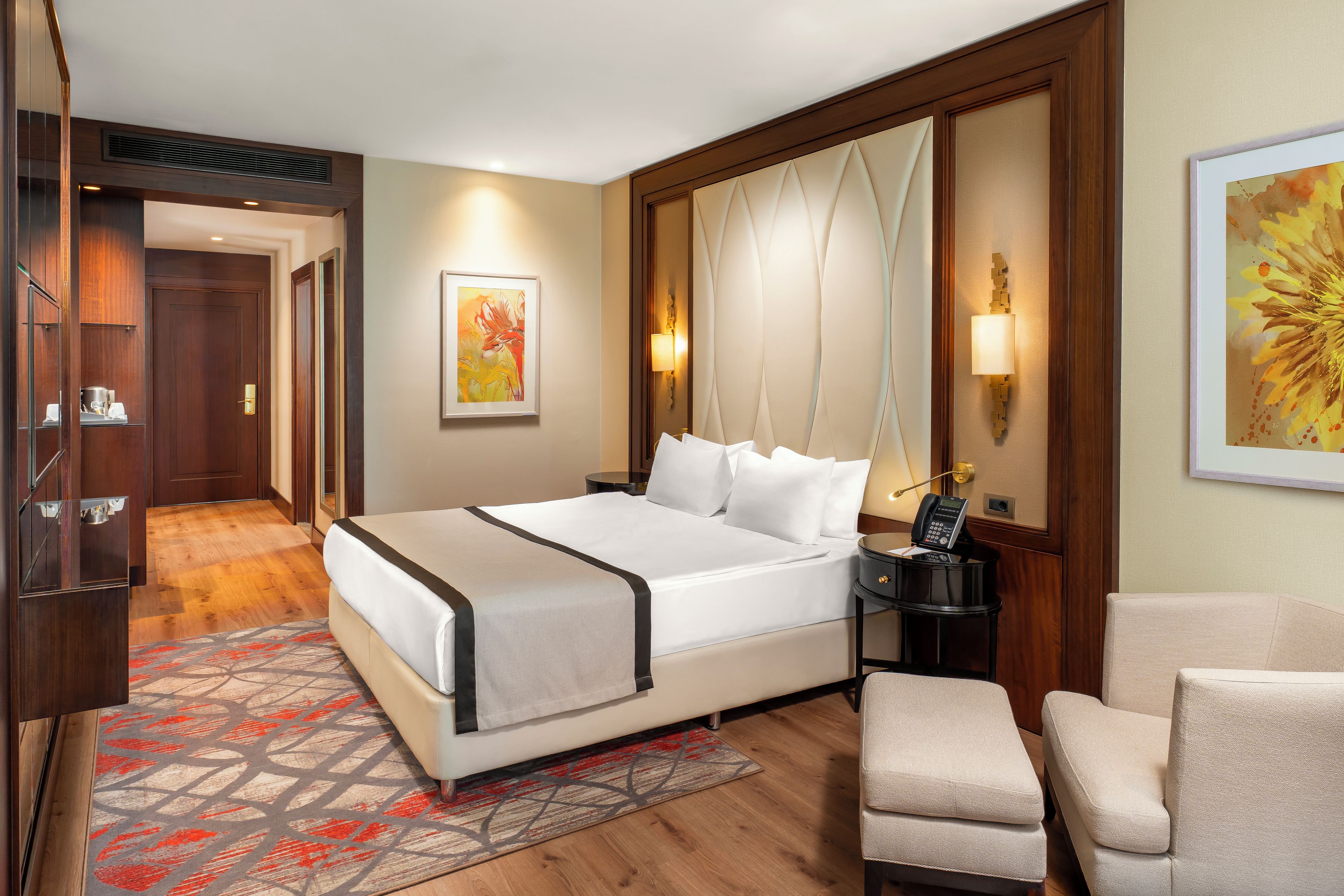 Una camera d'albergo con un letto grande, un comodino con una lampada, una sedia e un quadro appeso al muro.